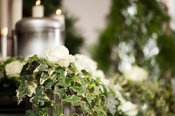 Nahaufnahme einer weißen Rose und Efeublättern auf einem Blumenarrangement mit Kerzen im Hintergrund.