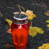 Rote Laterne steht auf dem Boden, umgeben von bunten Herbstblättern auf einer dunklen Oberfläche.