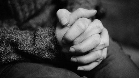 Nahaufnahme von zwei Händen, die ineinander verschränkt sind, vor einem unscharfen Hintergrund.